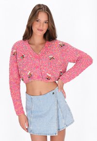 Rozā trikotāžas saīsināts kardigāns ar krāsainiem punktiņiem un ziedu akcentiem, ar dziļu V veida kakla izgriezumu un trim rozā pogām priekšpusē.