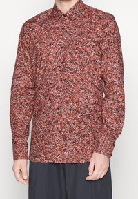 Camicia a fantasia floreale rossa con colletto button-down, maniche lunghe e bottoni neri su un tessuto texturizzato.