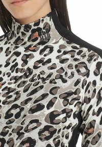 Leopardí vzor na topu s vysokým límcem v krémové a černé barvě, žebrovaná textura a kontrastní boční panely. Na límci je umístěno logo.
