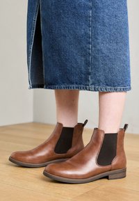 Bottines en cuir marron avec panneaux élastiques latéraux noirs et tirettes. Texture lisse, bout rond et talons empilés bas.