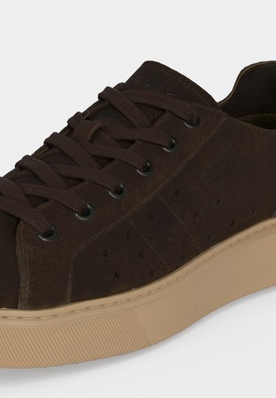 Σκούρο καφέ σουέντ αθλητικό παπούτσι με ταιριαστά κορδόνια, διάτρητα πλαϊνά πάνελ και μπεζ καουτσούκ σόλα σε απλό φωτεινό φόντο.