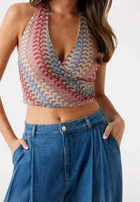 Hæklet halterneck-top med flerfarvet bølgemønster; parret med lyseblå højtaljede denimbukser med folder og sidelommer.