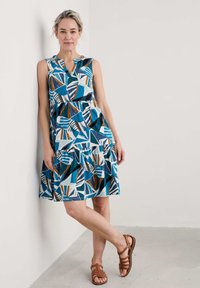 Blå och vit mönstrad klänning med lagerkjol och v-ringning, kombinerad med bruna sandaler med remmar. Slät tyg, avslappnad design.