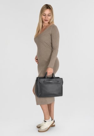 Borsa in pelle nera con doppio manico, forma strutturata e finiture in argento, abbinata a un vestito beige a coste e sneakers bianche.