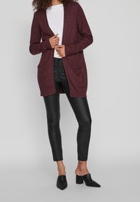 Burgundy neulejakko avoimella edessä, jossa on kaksi etutaskua, ribattu hihansuu ja helma. Yhdistetty mustiin nahkahousuihin ja mustiin avokkaisiin.