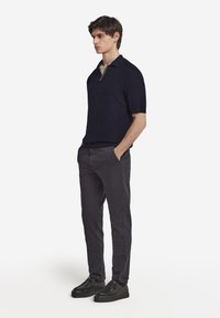 Marinblå stickad polo med kort ärm och dragkedjakrage, kombinerad med slim-fit mörkgrå byxor och svarta skor. Ren, modern silhuett.