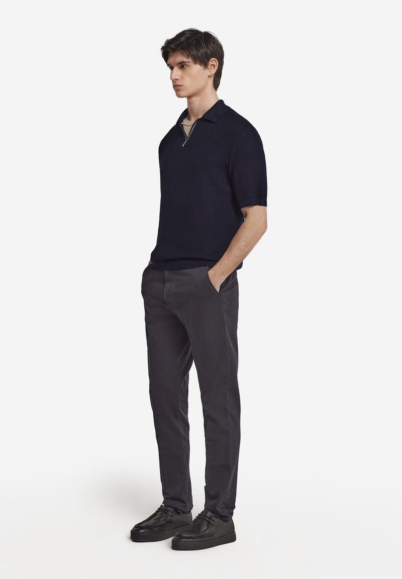 Marinblå stickad polo med kort ärm och dragkedjakrage, kombinerad med slim-fit mörkgrå byxor och svarta skor. Ren, modern silhuett.