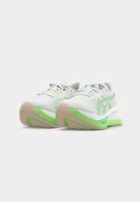 White athletic shoes with green accents, mesh upper, textured sole, and lightweight cushioning. Features lace-up design and logo detail.
