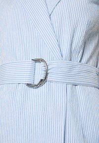 Robe à rayures verticales bleu clair et blanc avec une ceinture en tissu assortie attachée à la taille par une boucle en D argentée.