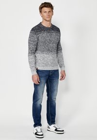 Grijs gradient gebreide trui met een ronde hals, lange mouwen en ribbels aan de mouwen, gecombineerd met lichtblauwe versleten jeans en zwart-witte sneakers.