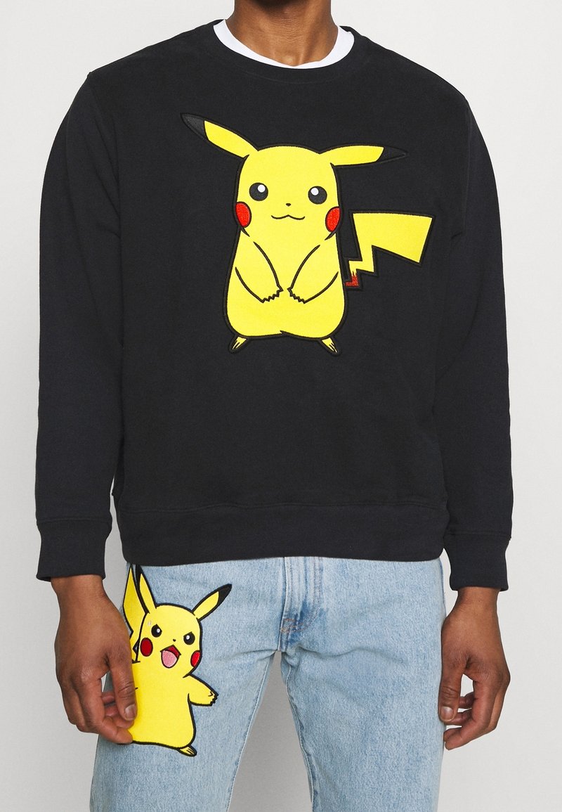 Felpa nera con grande grafica di Pikachu gialla sul davanti. Jeansazzurri chiari con un piccolo patch di Pikachu sul lato. Materiale in morbido cotone misto.