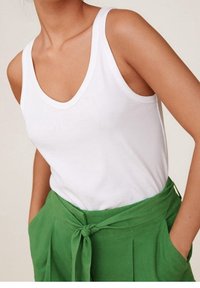 Bílý bezramínkový top s kulatým výstřihem, kombinovaný se zelenými vysokými kalhotami s páskem na zavázání a sklady.