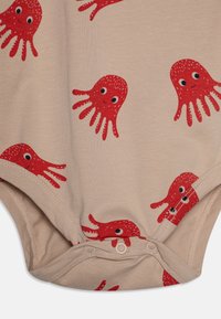 Combinaison beige avec des motifs de pieuvres rouges aux visages souriants, fabriquée en tissu doux, avec des fermetures à pression en bas pour un habillage facile.