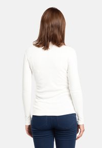 Maglietta bianca a maniche lunghe con un design aderente, texture liscia e scollo rotondo semplice, abbinata a jeans blu scuro.