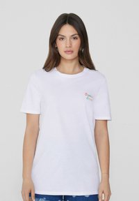 Camiseta de algodón blanca con cuello redondo, mangas cortas y bordado colorido que dice "Summer Lover" en el lado izquierdo del pecho. Corte casual.