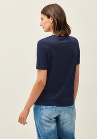 T-shirt bleu marine à manches courtes en mélange de coton doux, avec un col rond et un design minimaliste, associé à un jean en denim bleu clair.