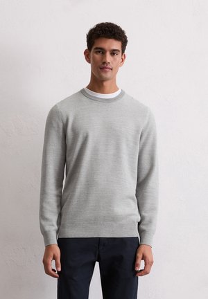 Grijze gebreide sweater met een ronde halslijn, gestructureerde stof en lange mouwen. Versterkt met een wit shirt eronder. Donkere broek.