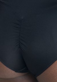 Black swimwear featuring a gathered seam at the back, made from stretchy material, with smooth texture and minimalistic design.