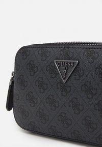 Portafoglio nero con texture, dotato di chiusura a zip, motivo con logo in rilievo e piastra triangolare con logo in metallo. Forma rettangolare compatta.