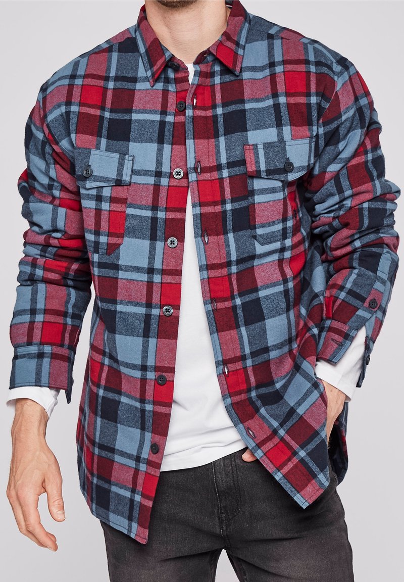 Röd och blå rutiga flanellskjortan med knäppning, två bröstfickor och kontrasterande tygtextur. Har knäppta manschetter.