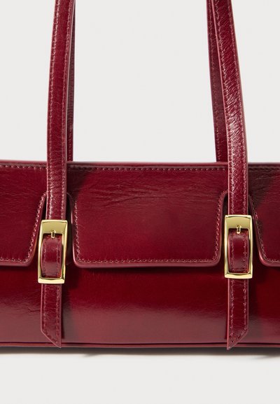 Μπορντό δερμάτινη τσάντα με γυαλιστερή φινίρισμα, διπλές λαβές και χρυσά κουμπώματα. Διαθέτει δομημένο σχέδιο και ελάχιστες λεπτομέρειες ραφής.