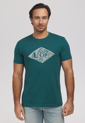 Mężczyzna w turkusowym T-shircie z krótkim rękawem z białym logo "Lee Cooper", w połączeniu z jasnoniebieskimi jeansami, stoi na jednolitym tle.