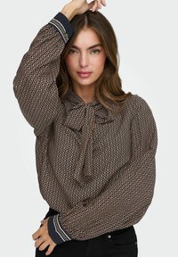 Blusa marrone con motivo a fantasia, colletto a fiocco, maniche lunghe a sbuffo e polsini rifiniti in blu navy. Presenta disegni circolari in oro e bianco.
