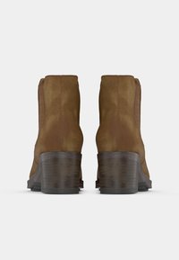 Bottes cheville en daim marron avec talons en bois empilés vues de dos sur fond blanc.