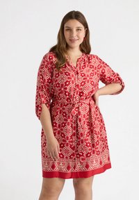 Red dress with floral patterns and white accents, featuring a collared neckline, short sleeves, and a tied waist detail. Smooth fabric texture.