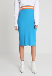 Jupe midi en tricot côtelé bleu avec une ceinture rayée orange et blanche, assortie à des bottines blanches. Texture lisse, design ajusté.