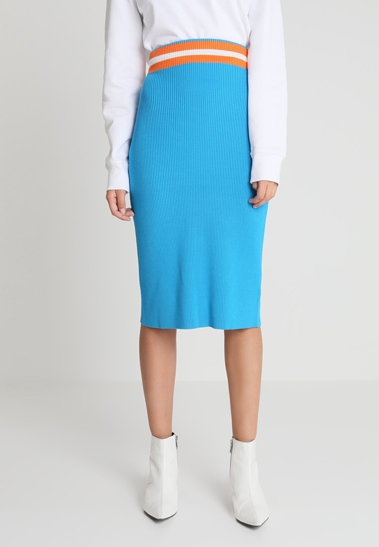 Jupe midi en tricot côtelé bleu avec une ceinture rayée orange et blanche, assortie à des bottines blanches. Texture lisse, design ajusté.