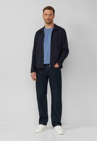 Marineblauwe zip-up jack over een lichtblauwe T-shirt, gecombineerd met donkere jeans en witte sneakers. Casual pasvorm met een soepele textuur. Eenvoudig ontwerp.