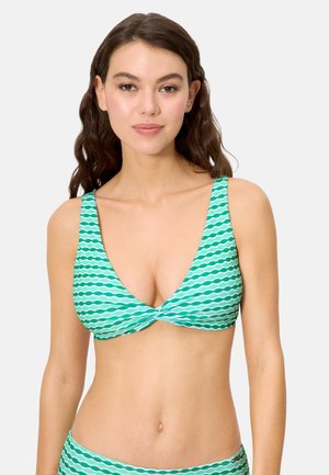 Mujer con cabello largo y ondulado de color castaño, con un top de bikini con el frente torcido y rayas de olas en tonos turquesa y blanco.