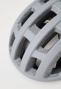 Grüner Fahrradhelm mit strukturierten Oberflächen, großen Belüftungsöffnungen und einer glatten Außenschale, die für Luftzirkulation und Sicherheit ausgelegt ist.
