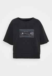 Musta lyhythihainen crop-paita, jossa on pyöreä pääntie, ja jossa on grafiikka VHS-nauhasta tekstillä. Pehmeää puuvillamateriaalia.