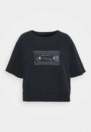 Musta lyhythihainen crop-paita, jossa on pyöreä pääntie, ja jossa on grafiikka VHS-nauhasta tekstillä. Pehmeää puuvillamateriaalia.