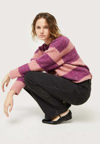 Suéter a rayas en rosa y púrpura, confeccionado en tejido de punto texturizado. Combinado con jeans ajustados negros y zapatos Mary Jane negros.