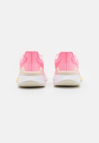 Vaaleanpunaiset urheilukengät, joissa on verkko-osa, pehmustettu nilkkaosa ja valkoinen ulkopohja. Ominaisuuksiin kuuluu joustava muotoilu ja huomaamattomat keltaiset yksityiskohdat.