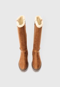 Καφέ μποτάκια μέχρι το γόνατο από σουέτ, με μαλακή κρεμ φόδρα στην κορυφή και καφέ καουτσούκ σόλα.