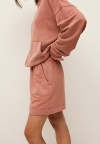 Sudadera rosa y pantalones cortos a juego hechos de tela suave, con bolsillo delantero, cintura elástica y ajuste relajado.