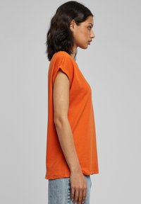 Oranje T-shirt met korte mouwen van zachte stof, met een losse pasvorm en opgerolde mouwen. Gecombineerd met lichtblauwe spijkerbroek.