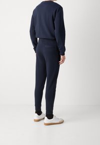 Navy blauwe sweatshirt en bijpassende joggers, beide van zacht materiaal, met een cropped ontwerp, ribgebreide manchetten en een achterzak op de broek.