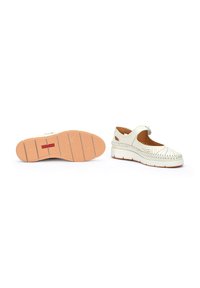 Chaussures en cuir blanc avec un design perforé, une sangle velcro et une semelle rembourrée. La semelle extérieure présente une surface texturée de couleur marron clair.
