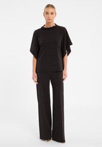 Ensemble noir texturé en deux pièces avec un pantalon à jambes larges et un haut à manches chauve-souris. Le tissu a un subtil éclat dans l'ensemble.