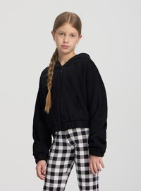 Felpa nera corta con tasca frontale e cappuccio, abbinata a leggings a quadri bianchi e neri. Tessuto liscio e polsini elastici.