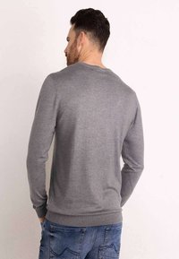 Grijze gebreide trui met een ronde halslijn en geribbelde manchetten, weergegeven vanaf de achterkant, met een gladde textuur en aansluitend ontwerp.