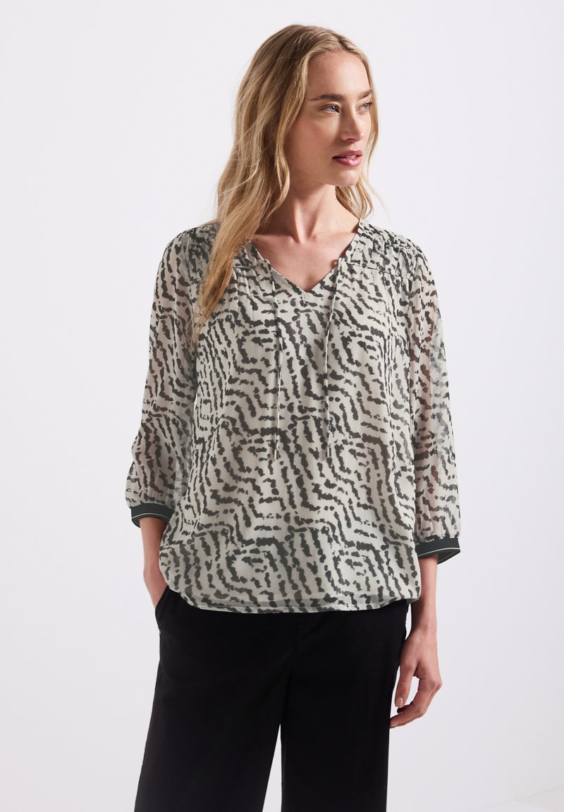 Blusa trasparente a fantasia con scollatura a V, maniche lunghe con dettagli arricciati e una palette di colori muted in nero e grigio chiaro.