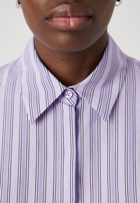 Lavender striped shirt with a classic collar, featuring black vertical stripes and a small lavender button at the neck. Smooth, lightweight fabric.