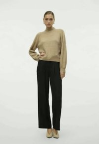 Μπεζ πλεκτό πουλόβερ με μακριά μανίκια, συνδυασμένο με μαύρα παντελόνια ψηλής μέσης και μπεζ παπούτσια με μυτερή μύτη. Απλός, εφαρμοστός σχεδιασμός.