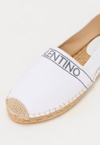 Valkoinen kanvaespadrille, jossa on pyöreä varvas, ja siinä on kudottu juuttipohja sekä harmaalla brodeerattu "VALENTINO"-logo yläreunassa.